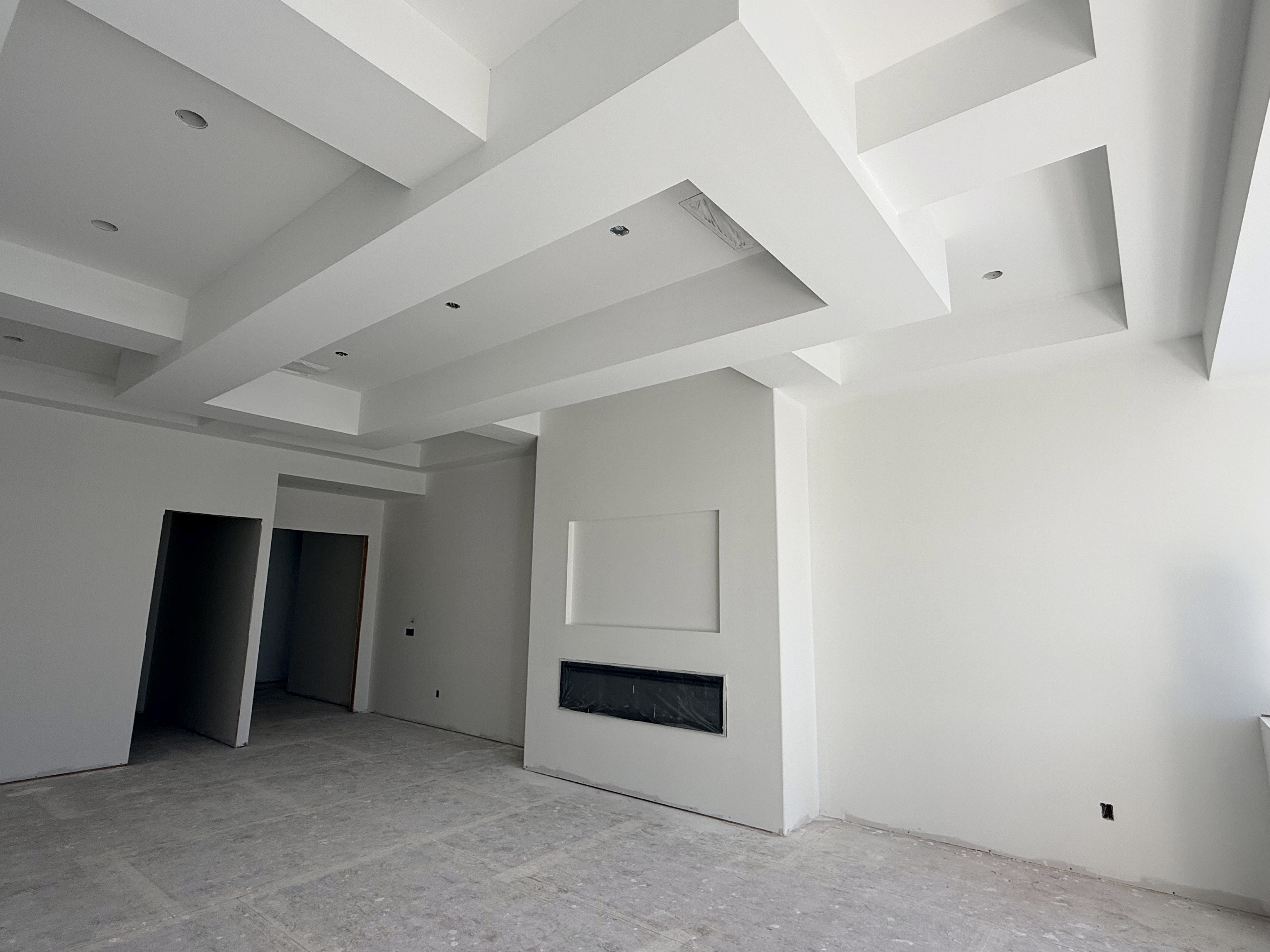 New build: great room with stepped tray ceilings and a drywall fireplace wall